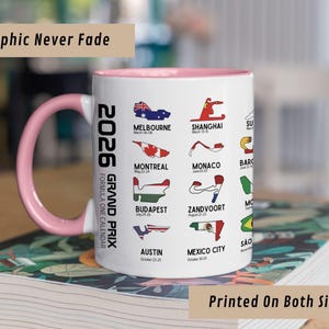Peut inclure: Un mug en c&eacute;ramique blanc avec un int&eacute;rieur et une anse roses, pr&eacute;sentant un calendrier du Grand Prix de Formule 1 2026. Le mug affiche des trac&eacute;s de circuits et des noms de villes comme Melbourne et Austin. Le texte sur le mug indique "Graphic Never Fade" et "Printed On Both Sides."