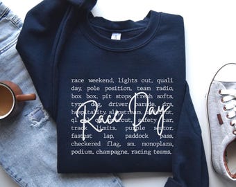 May include: A navy blue sweatshirt with the words "Race Day" in a cursive font. The sweatshirt has a crew neck and long sleeves. The text includes racing terms like "pole position" and "checkered flag".