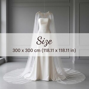 May include: A white floor-length bridal cape featuring a sheer tulle fabric adorned with scattered pearls and intricate beaded embroidery at the neckline. The cape measures 118.11 x 118.11 inches and is displayed over a simple strapless white gown.