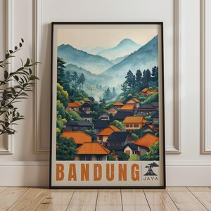 May include: A framed travel poster featuring a landscape of Bandung, Java, with orange-roofed houses nestled among green trees and misty blue mountains in the background. The text BANDUNG and JAVA is printed in large orange letters at the bottom.