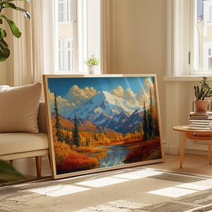 May include: A rectangular framed landscape painting featuring a snow-capped mountain peak rising above a valley with golden autumn trees, evergreen pines, and a reflective blue river under a bright sky with soft clouds, displayed in a light wood frame.