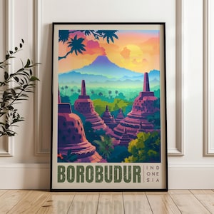 Op de afbeelding: Een ingelijste kunstdruk met een kleurrijke illustratie van het Borobudur-tempelcomplex in Indonesië. De scène toont paarse stoepa's te midden van weelderige groene bomen onder een levendige zonsonderganghemel met een bergsilhouet en de tekst BOROBUDUR IND ONE SIA.