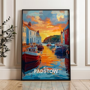 Puede incluir: Una impresión artística enmarcada del puerto de Padstow al atardecer. La obra presenta coloridos barcos, edificios y agua que refleja los tonos naranja y azul del cielo. La palabra "PADSTOW" está impresa en la parte inferior.