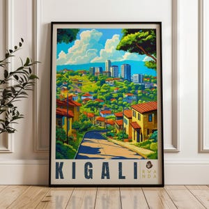 May include: A framed travel poster featuring a vibrant illustration of Kigali, Rwanda. The artwork depicts a winding road leading toward a cityscape with modern buildings, lush green hills, and houses with orange roofs under a bright blue sky.