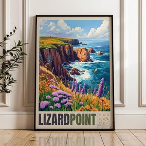 May include: A framed vertical art print featuring a coastal landscape with steep cliffs, blue ocean waves, and a field of purple and yellow wildflowers in the foreground. The text LIZARD POINT CORNWA is printed in bold letters at the bottom of the print.