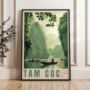Könnte beinhalten: Ein gerahmtes Reiseplakat mit einer grün gehaltenen Illustration von Tam Coc, Vietnam. Das Bild zeigt kleine Boote mit Personen in konischen Hüten auf einem Fluss, umgeben von Kalksteinfelsen und Blattwerk, mit dem Text TAM COC VIETNAM.