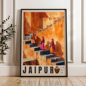 May include: Framed art print featuring three women in colorful saris carrying water jugs up a staircase. The artwork has a warm color palette of oranges and browns, with the word "JAIPUR" and a pot graphic at the bottom.
