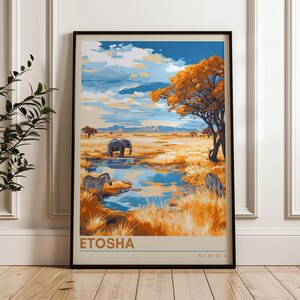 A framed poster of Etosha, Namibia, showcasing a picturesque savannah scene. It features zebras grazing, an elephant near a reflective waterhole, and a striking orange acacia tree under a dramatic, cloud-filled sky with distant mountains.