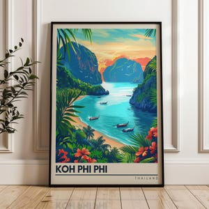 May include: A framed travel poster featuring a vibrant illustration of Koh Phi Phi, Thailand. The artwork depicts turquoise waters, limestone cliffs, tropical palm leaves, and red hibiscus flowers, with the text KOH PHI PHI THAILAND at the bottom.
