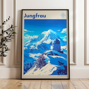 Może przedstawiać: Oprawiony plakat podróżniczy przedstawiający górę Jungfrau w Szwajcarii. Plakat ma niebiesko-białą kolorystykę, ze słowem "Jungfrau" na górze. Budynek z kopułą znajduje się na ośnieżonym szczycie. Słowo "Szwajcaria" znajduje się na dole.