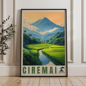 May include: A framed vertical poster featuring a landscape illustration of Mount Ciremai in Java. The scene depicts a blue mountain peak above lush green rice terraces and a winding river. The text CIREMAI and JAVA with a volcano icon appear below.