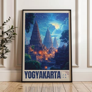 Op de afbeelding: Een ingelijste print met een nachtscène van het Yogyakarta-tempelcomplex. Het kunstwerk toont hoge structuren verlicht door warme lichten tegen een achtergrond van een sterrenhemel en wolken. Het woord "YOGYAKARTA" staat onderaan.