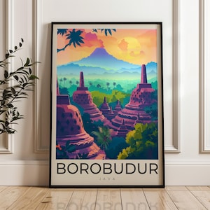 Op de afbeelding: Een ingelijste verticale kunstdruk met een kleurrijke illustratie van de Borobudur-tempel op Java. De scène toont paarse stoepa's te midden van weelderige groene bomen onder een zonsonderganghemel met een grote gele zon en een blauwe berg.