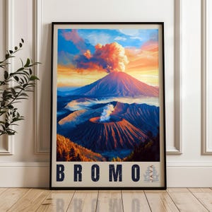 May include: A vertical framed wall art print depicting Mount Bromo in Java, Indonesia. The scene features a volcanic landscape with a smoking crater, a large mountain peak, and a vibrant sunset sky. The text BROMO JAVA is printed at the bottom.