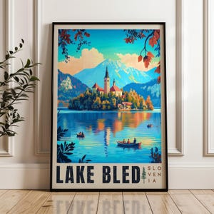 Può includere: Un poster da viaggio incorniciato con una vivace illustrazione del lago di Bled in Slovenia. L'opera raffigura una chiesa su un'isola, acqua blu con piccole barche e montagne in lontananza sotto un cielo luminoso. Il testo recita LAKE BLED SLOVENIA.