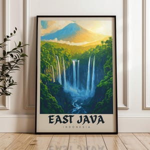 May include: A framed vertical wall art print featuring a landscape illustration of East Java, Indonesia. The artwork depicts a large mountain peak above a lush green forest with multiple cascading waterfalls flowing into a river. Text reads EAST JAVA INDONESIA.
