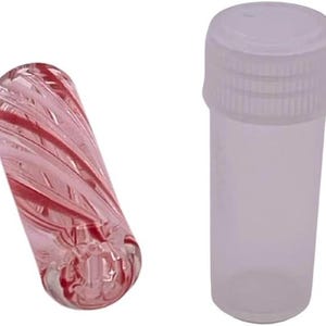 May include: A clear, cylindrical vial with a white cap next to a pink glass object. The glass object has a spiral design with red accents. The vial is empty and has a screw-on cap.