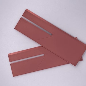 Op de afbeelding: Twee roze rechthoekige objecten met een sleuf in het midden. De objecten overlappen elkaar lichtjes, waarbij de bovenste de onderste gedeeltelijk bedekt. Ze hebben een matte afwerking en staan tegen een witte achtergrond.