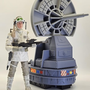 May include: A plastic action figure dressed in a white and tan cold-weather uniform with green goggles, holding a black blaster rifle. Beside the figure stands a large, gray, circular radar dish mounted on a tracked, multi-colored base.