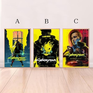 May include: Three framed Cyberpunk 2077 posters. The posters feature vibrant yellow and black color schemes with futuristic character designs and the game's logo. The posters are displayed on a light wood surface.