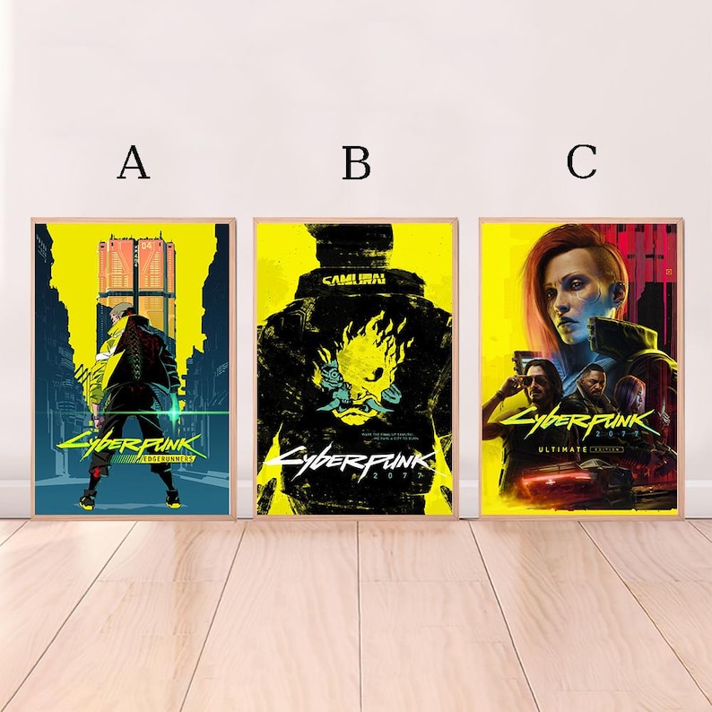 May include: Three framed Cyberpunk 2077 posters. The posters feature vibrant yellow and black color schemes with futuristic character designs and the game's logo. The posters are displayed on a light wood surface.