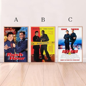 May include: Three framed movie posters for the Rush Hour film series. The posters feature Jackie Chan and Chris Tucker. The posters have a wooden frame and are displayed against a white wall.