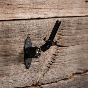 Puede incluir: Soporte de pared de metal negro con un brazo giratorio para colgar una guitarra. El soporte está fijado a una pared de madera.