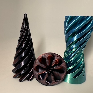 以下が含まれることがあります： 3Dプリントされたオブジェクト3つ。濃い茶色の螺旋模様の円錐形、ターコイズブルーと青の螺旋模様の壺、濃い茶色の花のような模様の円盤形