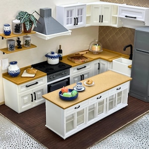 Peut inclure: Un ensemble de cuisine miniature comprenant des armoires blanches avec des poignées noires, un plan de travail beige, une hotte grise et un réfrigérateur gris. La cuisine inclut une cuisinière, un évier, un îlot, des étagères et des aliments.
