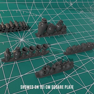 Może przedstawiać: Kolekcja miniaturowych wyrobów ceramicznych, w tym dzbanów, dzbanów i filiżanek, wystawionych na szarym kwadratowym talerzu. Elementy są pokazane na kwadratowym talerzu o wymiarach 1x1 cm.
