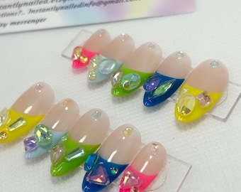 May include: Set of ten press-on nails with a variety of colorful designs and rhinestones. The nails are arranged on a clear plastic display card. The card has the text "Instantly Nailed" printed on it.