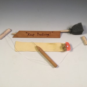 May include: A leatherworking kit with a wooden awl, a piece of leather, a wooden tool with a sponge on the end, and a wooden sign that says "Keep Practicing!"