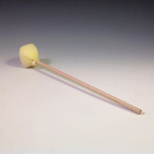 May include: A wooden craft stick with a yellow sponge attached to the end. The sponge is round and has a slightly pointed tip.