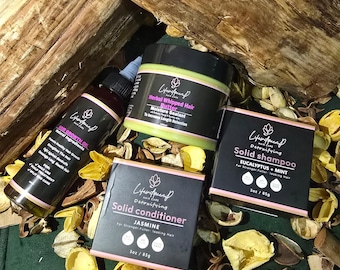 Op de afbeelding: Een verzameling haarverzorgingsproducten, waaronder haargroeiolie, opgeklopte haarboter, vaste shampoo en vaste conditioner. De producten zitten in zwarte containers met witte en roze accenten, met de tekst "LifeFaced".