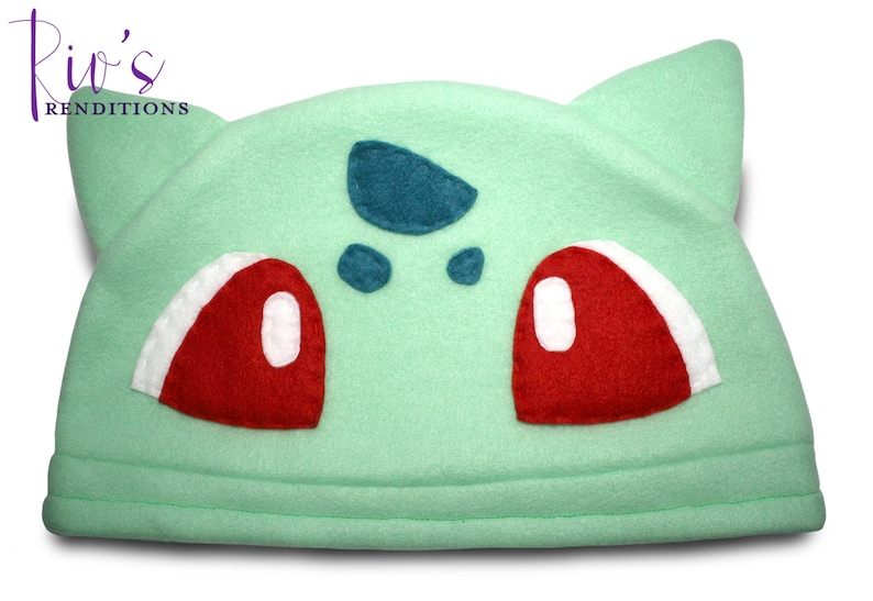 Pu&ograve; includere: Un cappello in pile verde chiaro che assomiglia a un personaggio di Bulbasaur. Il cappello presenta dettagli occhi rossi e bianchi, macchie turchesi e orecchie a punta. Il testo "Riv's Renditions" &egrave; nell'angolo in alto a sinistra.