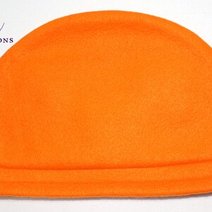 May include: Bright orange fleece beanie hat. The hat has a rounded top and a folded brim. The text "Rio's Renditions" is in the upper left corner in purple script.