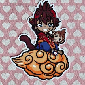 May include: A sticker featuring an anime-style character with a monkey companion, seated on a stylized orange cloud. The character wears a red outfit and a red headband. The background is pink with white hearts.