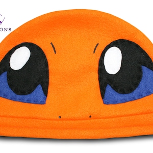May include: An orange fleece hat featuring a cartoon character's face. The hat has large black eyes with white highlights and blue accents, and a small mouth. The text "Rio's Renditions" is in the upper left corner.