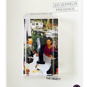 Puede incluir: Imagen de la portada del álbum "Presence" de Led Zeppelin, encapsulada en plástico transparente. La imagen muestra a una pareja y un niño en un barco. El fondo es una escena portuaria con barcos. El texto "THE OBJECT" está en la parte inferior.