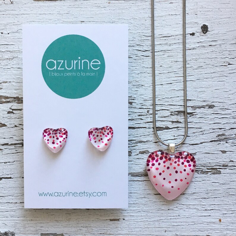 May include: A jewelry set featuring a pink heart pendant necklace and matching heart stud earrings. The hearts are decorated with red and pink polka dots. The set is displayed on a white card with the text "azurine | bijoux peints &agrave; la main !" and the website address.