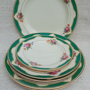 Peut inclure: Un ensemble de quatre assiettes en céramique blanche avec un motif floral vert et or. Les assiettes sont empilées les unes sur les autres.