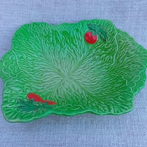 Op de afbeelding: Een groene keramische serveerschaal in de vorm van een slablaadje met twee rode tomaten. De schaal is perfect om salades of snacks te serveren.