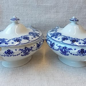 Op de afbeelding: Twee witte porseleinen serveerschalen met blauwe bloemenmotieven. De schalen hebben deksels en zijn ovaal.