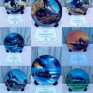 Può includere: Una collezione di nove piatti decorativi blu e dorati con locomotive a vapore d'epoca in vari paesaggi. Ogni piatto è accompagnato da un certificato di autenticità con il testo "Orient Express" stampato su di esso.