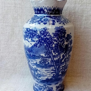 May include: A blue and white porcelain vase with a scalloped rim and a floral and landscape design. The vase features a scene of people fishing in a river.