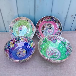 May include: Four decorative ceramic bowls with floral designs. The bowls feature a variety of colours, including green, pink, blue, and purple. Each bowl has a gold rim and a detailed floral pattern on the interior and exterior.
