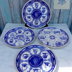 May include: A collection of blue and white decorative plates. The plates feature various jug designs and the text "THE DECORATIVE JUG COLLECTION". One plate is oval-shaped, and another has a 1996 date. The plates are displayed on a white surface.