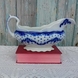 May include: A white porcelain gravy boat with a blue and white floral pattern. The boat has a scalloped edge and a handle.