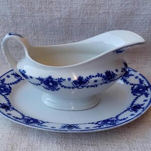 May include: A white porcelain gravy boat with a blue floral design and a matching saucer. The boat has a handle and a spout.