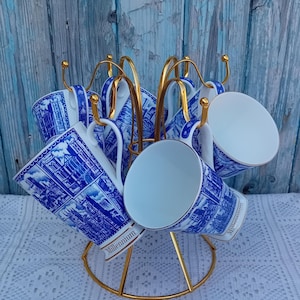 May include: A set of six white ceramic mugs with blue and gold designs. The mugs are displayed on a gold metal stand. The mugs feature a blue and white design with the word "Millennium" printed on the side.